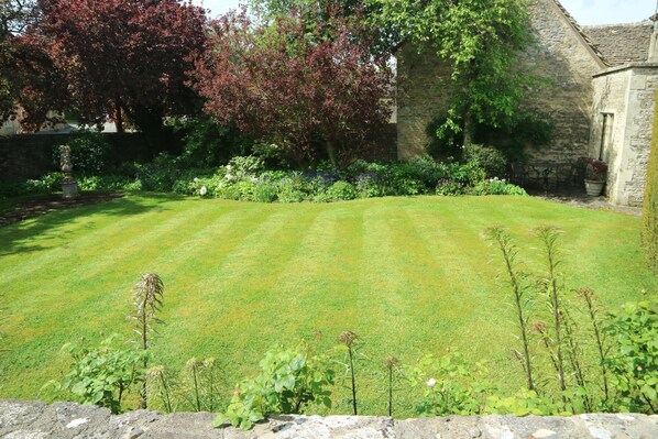 A well-maintained lawn with a stone wall in the foreground and a stone building in the background.