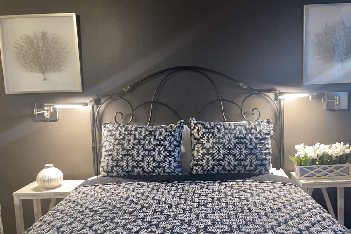 A bedroom with a patterned bedspread, two matching pillows, a metal headboard, bedside tables with lamps, and framed artwork on the walls.