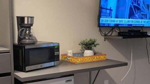 Una kitchenette compacta con microondas, cafetera y refrigerador pequeño. Un televisor de pantalla plana está montado en la pared sobre la encimera.