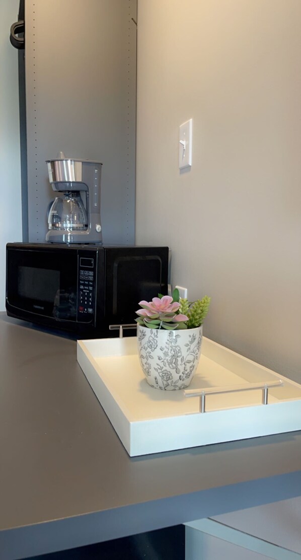 A kitchen counter with a microwave, a coffee maker, and a floral pot.