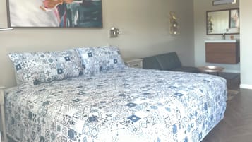 Un dormitorio con una colcha estampada, un cuadro abstracto grande en la pared, una mesita de noche y un buró.