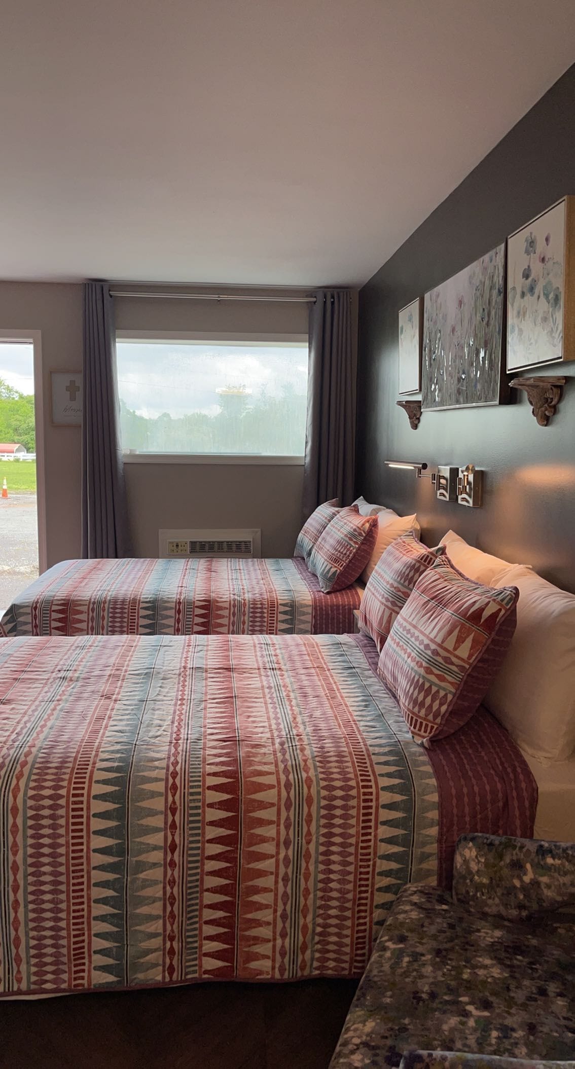 A bedroom with a large bed, a bedside table, a window with curtains, and wall-mounted artwork.