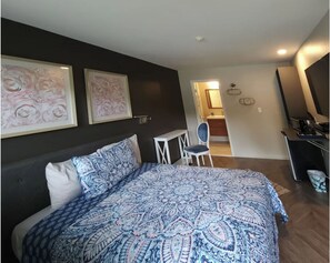 A bedroom with a large bed, a desk, and a chair. There are two framed artworks on the wall. - Hotel Lake Anna (Spotsylvania)