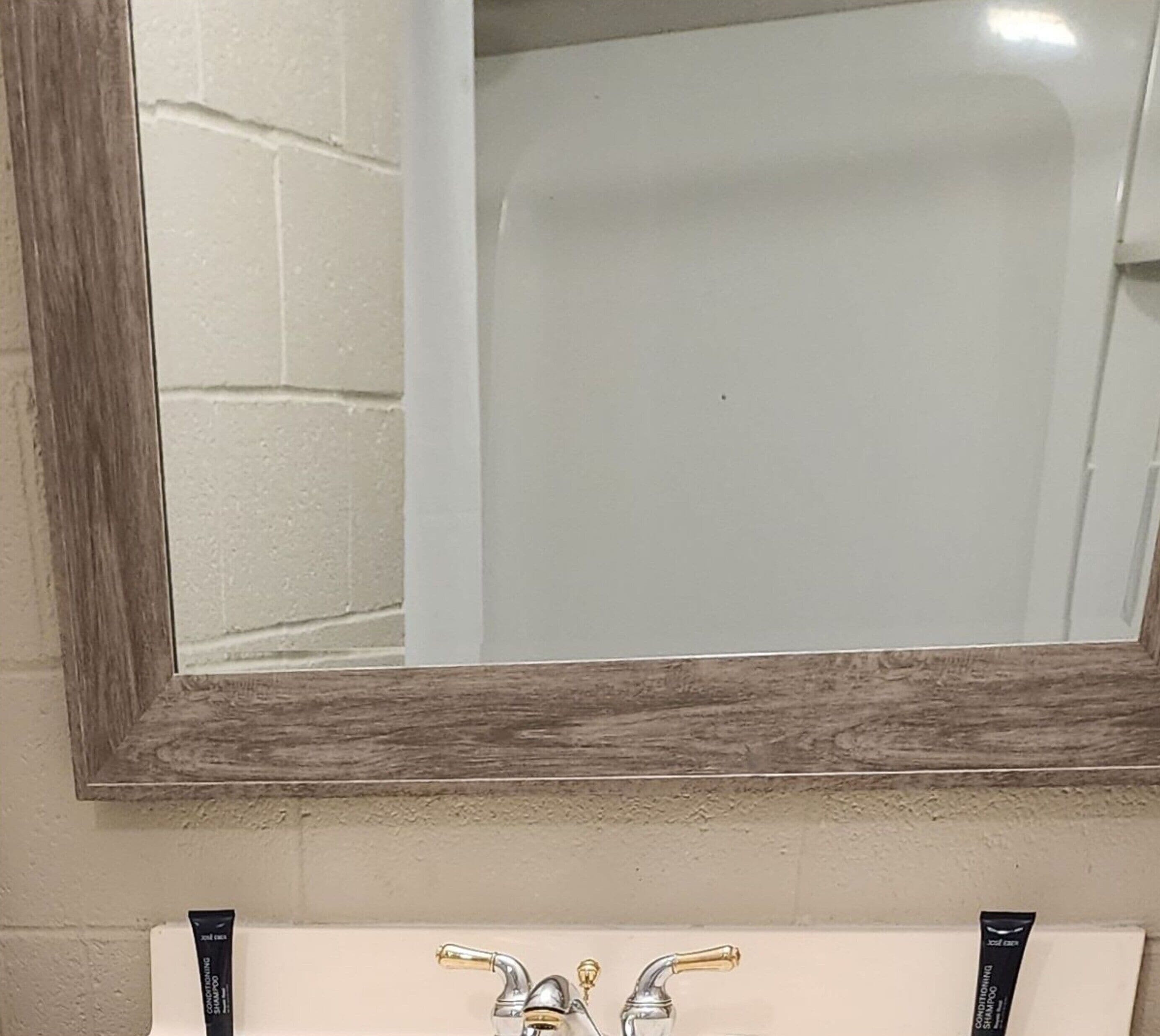 Une salle de bain avec un miroir encadré en bois, un lavabo blanc et deux robinets de couleur or.
