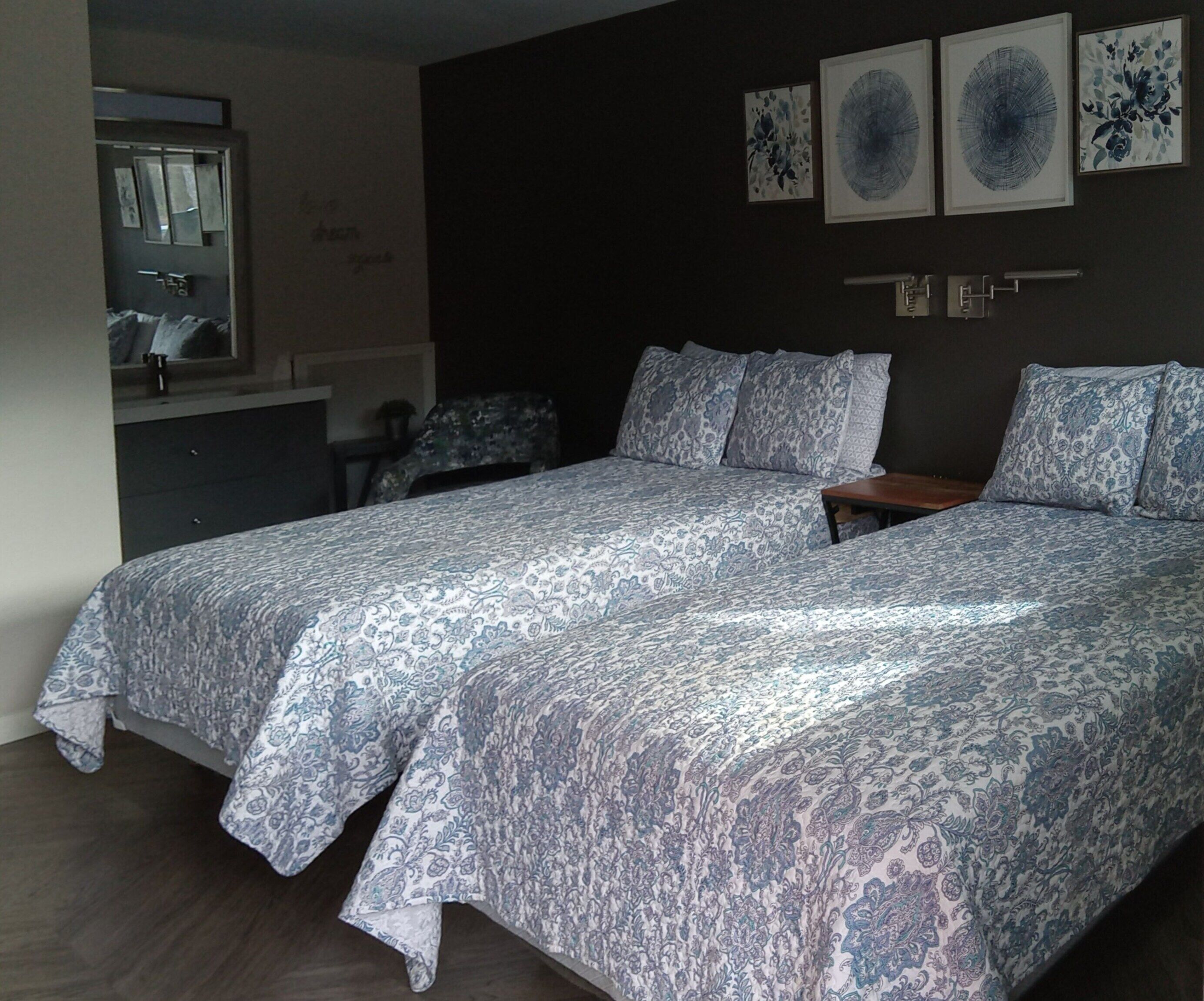 Une chambre avec deux lits, une commode, un miroir et trois œuvres d’art encadrées accrochées au mur.