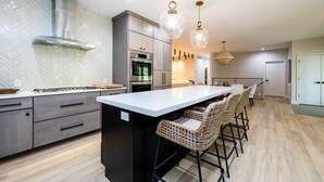 A modern kitchen with a central island, stainless steel appliances, and a herringbone-patterned backsplash. - (2027 OPEN!) Gorgeous Grand Beach Home With Private Pool! (Grand Beach)