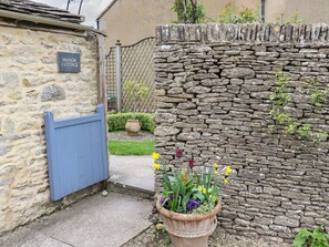 A stone cottage with a blue gate, a sign reading "Manor Cottage," and a flower pot with daffodils. - Manor Cottage (Cirencester)