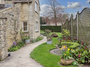 A stone building with a paved pathway leading to a garden with various plants and flowers. - Manor Cottage (Cirencester)