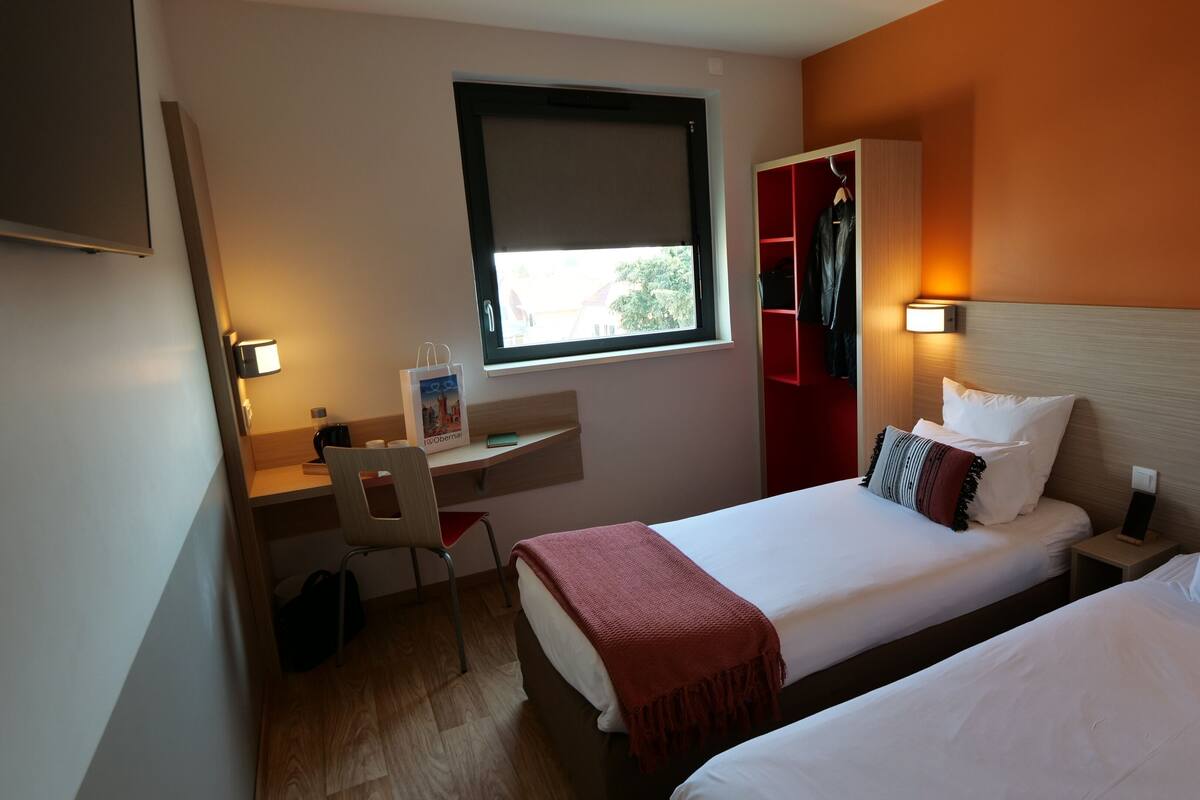 A hotel room with a bed, a desk, a chair, a wardrobe, and a window.