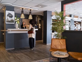 Zona de recepción con mostrador, recepcionista, cliente y área de espera con una silla y una mesa.