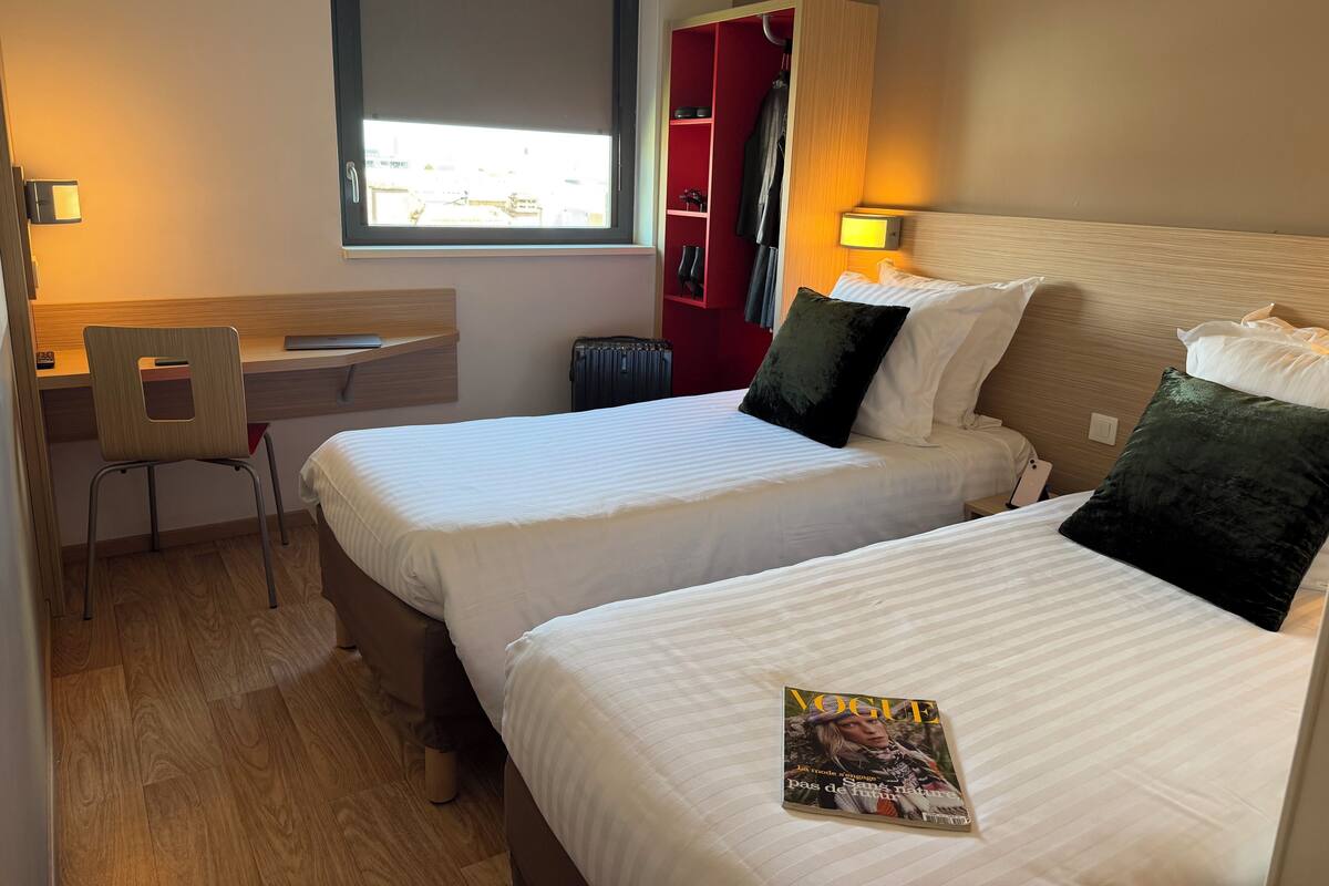 A hotel room with two beds, a desk, and a chair.