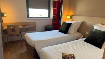 Quarto de hotel com duas camas, uma escrivaninha e uma cadeira.
