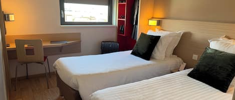 A hotel room with two beds, a desk, and a chair.