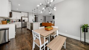 A modern kitchen with white cabinets, a wooden dining table, and a unique light fixture.