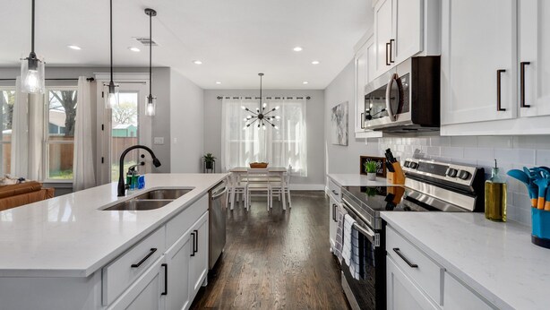 A modern kitchen with white cabinetry, a central island, stainless steel appliances, and pendant lighting.