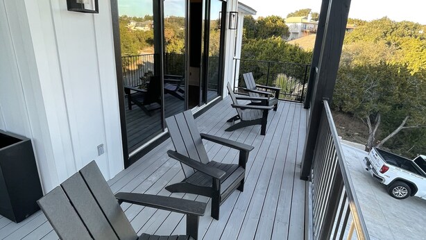 Une terrasse extérieure couverte, équipée de quatre fauteuils Adirondack, d’une petite table et d’un véhicule blanc garé à l’extérieur.