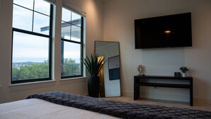 Une chambre avec un grand lit, un téléviseur fixé au mur, un miroir et une fenêtre donnant sur un paysage verdoyant.