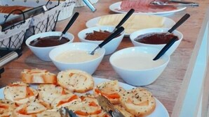Une table de buffet proposant divers aliments, notamment du pain, des sauces et des viandes en tranches.