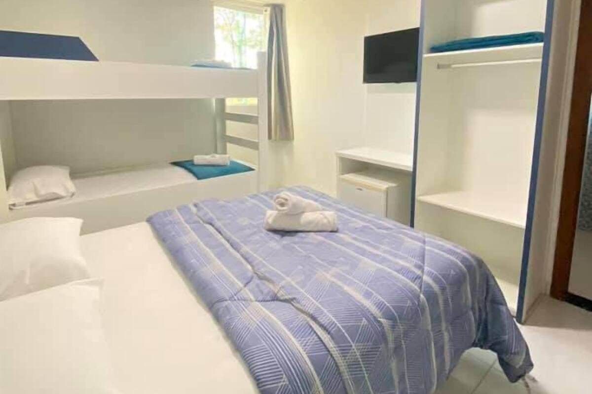 Ein Hotelzimmer mit Etagenbett, Einzelbett, Kleiderschrank und kleinem Schreibtisch.