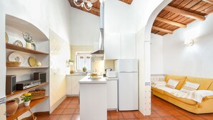 A compact kitchen with white cabinets, a central island, and a yellow sofa in the adjacent living area.