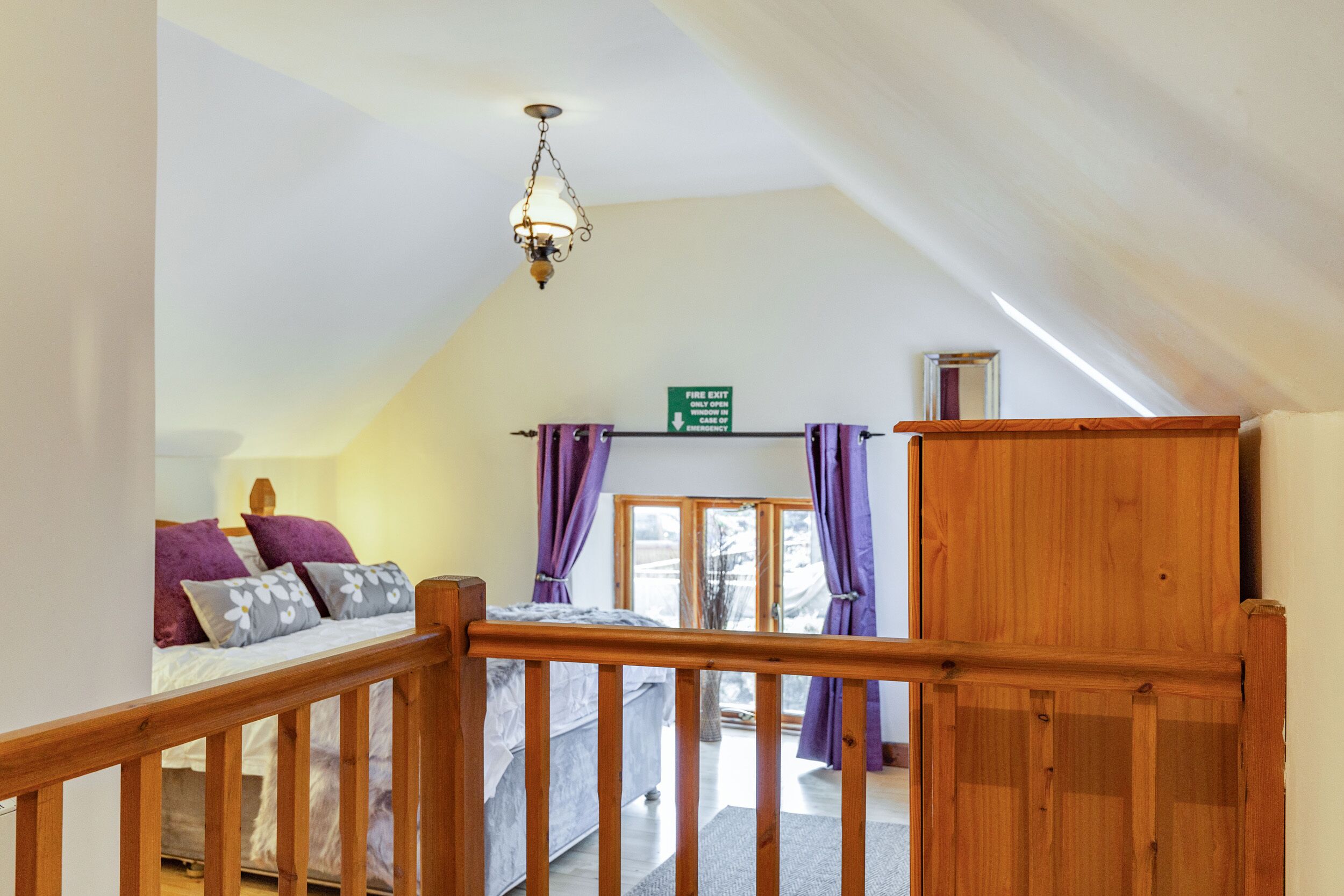 Ein Schlafzimmer mit einem Holzbett, einem Nachttisch, einer Lampe und einem Blick ins Freie durch ein Fenster.