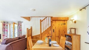 A dining area with a wooden table set for two, a sofa, and a staircase leading to another level. - Miller's Lodge (Liskeard)