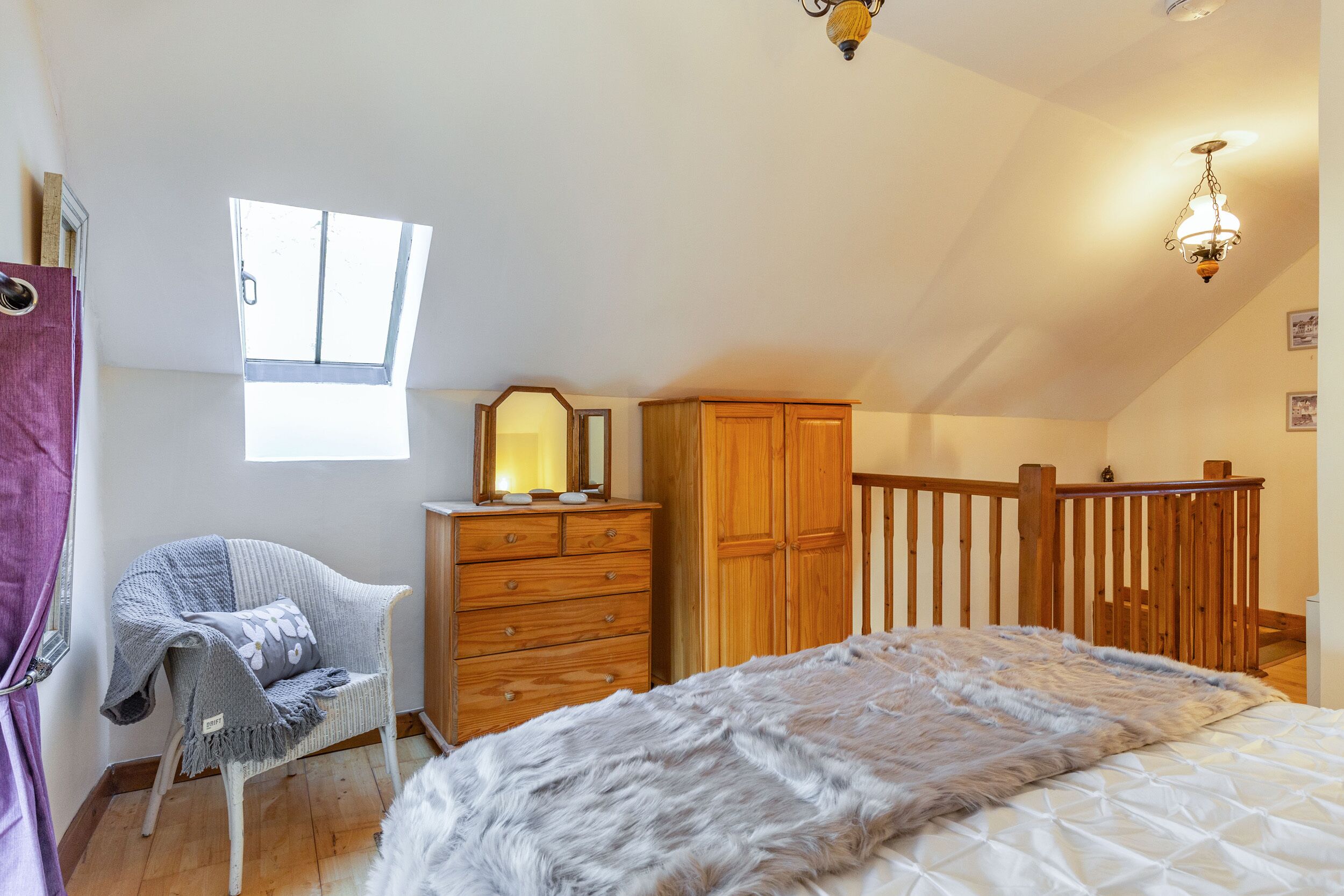 A bedroom with a bed, a wooden wardrobe, a dresser, a chair, a window, and a chandelier.