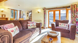 A cozy living room with a brown sofa, a wooden coffee table, and a chair with floral cushions. - Miller's Lodge (Liskeard)