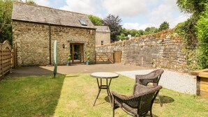 A stone building with a door, a small table, and two wicker chairs in a grassy area. - Miller's Lodge (Liskeard)