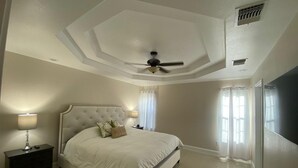 Een slaapkamer met een groot bed, een plafondventilator en een nachtkastje met een lamp.