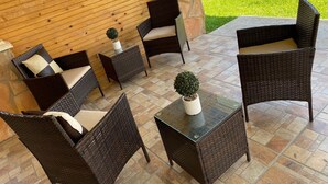 Een terras met buitenmeubilair van riet, een tafeltje met een plant in pot en een vuurkorf van steen op de achtergrond.