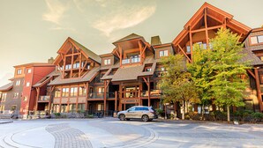 A multi-story lodge with a central atrium, outdoor seating, and a car parked in front. - "Evergreen" at Solara Resort (Canmore)