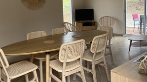 A dining area with a wooden table and wicker chairs, a television, and a view of the outdoors. - 6/8 person gîte with swimming pool and jacuzzi (Thésée)