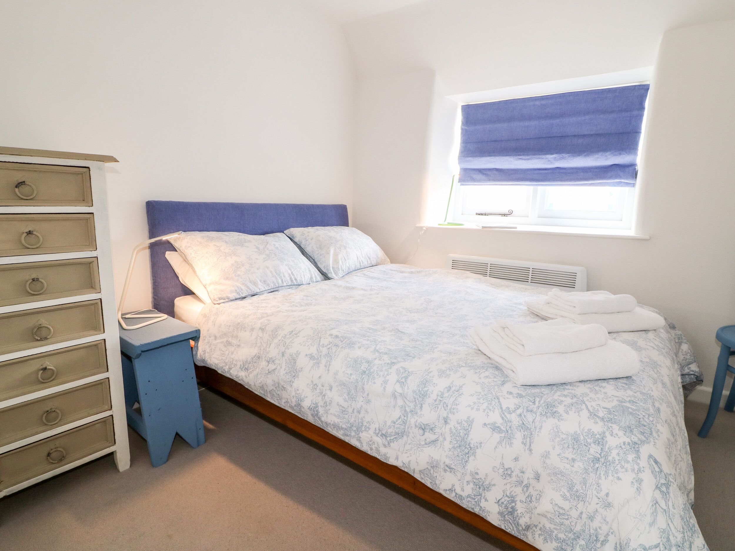 A bedroom with a bed, a dresser, a nightstand, and a window with a blind.