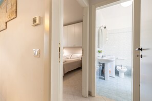 Un dormitorio con cama, un baño con lavamanos e inodoro, y una puerta que da a otra habitación.