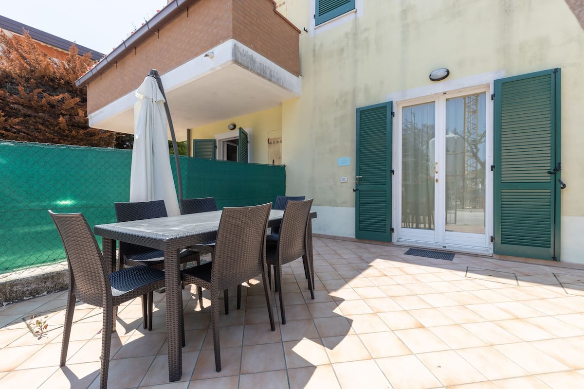 Une terrasse extérieure avec une table et des chaises, un parasol et une clôture verte.