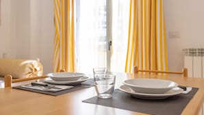 Una mesa de comedor dispuesta con platos, vasos y cubiertos, con cortinas amarillas al fondo.