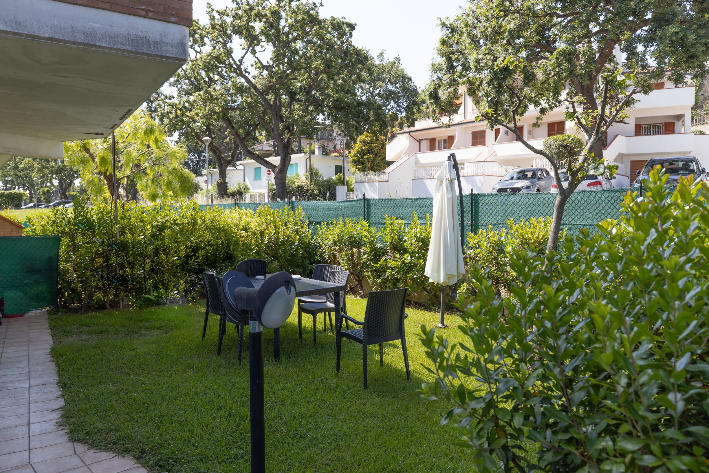 A patio area with a table and chairs, surrounded by greenery and a fence.
