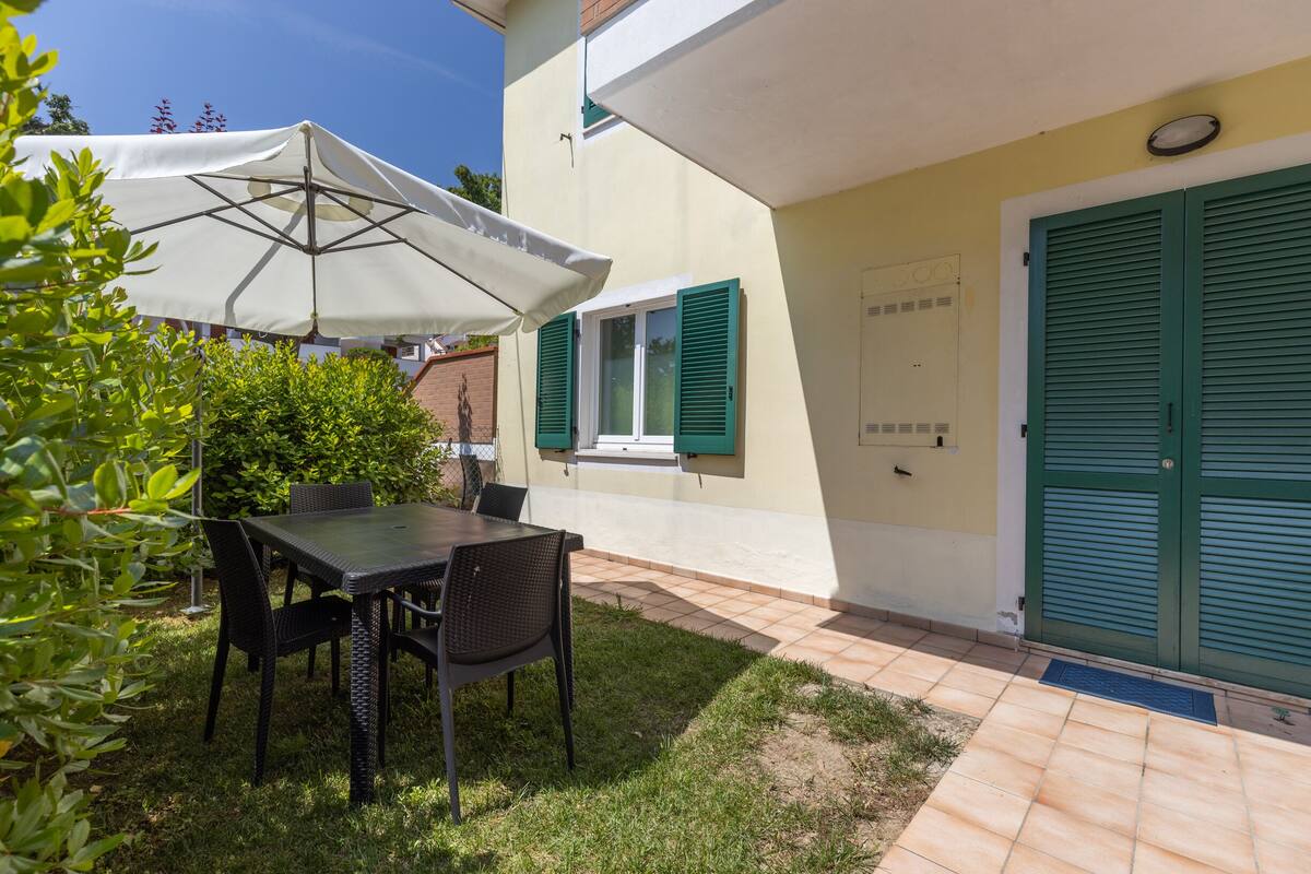 Une terrasse avec une table et des chaises, un parasol blanc et une porte verte.