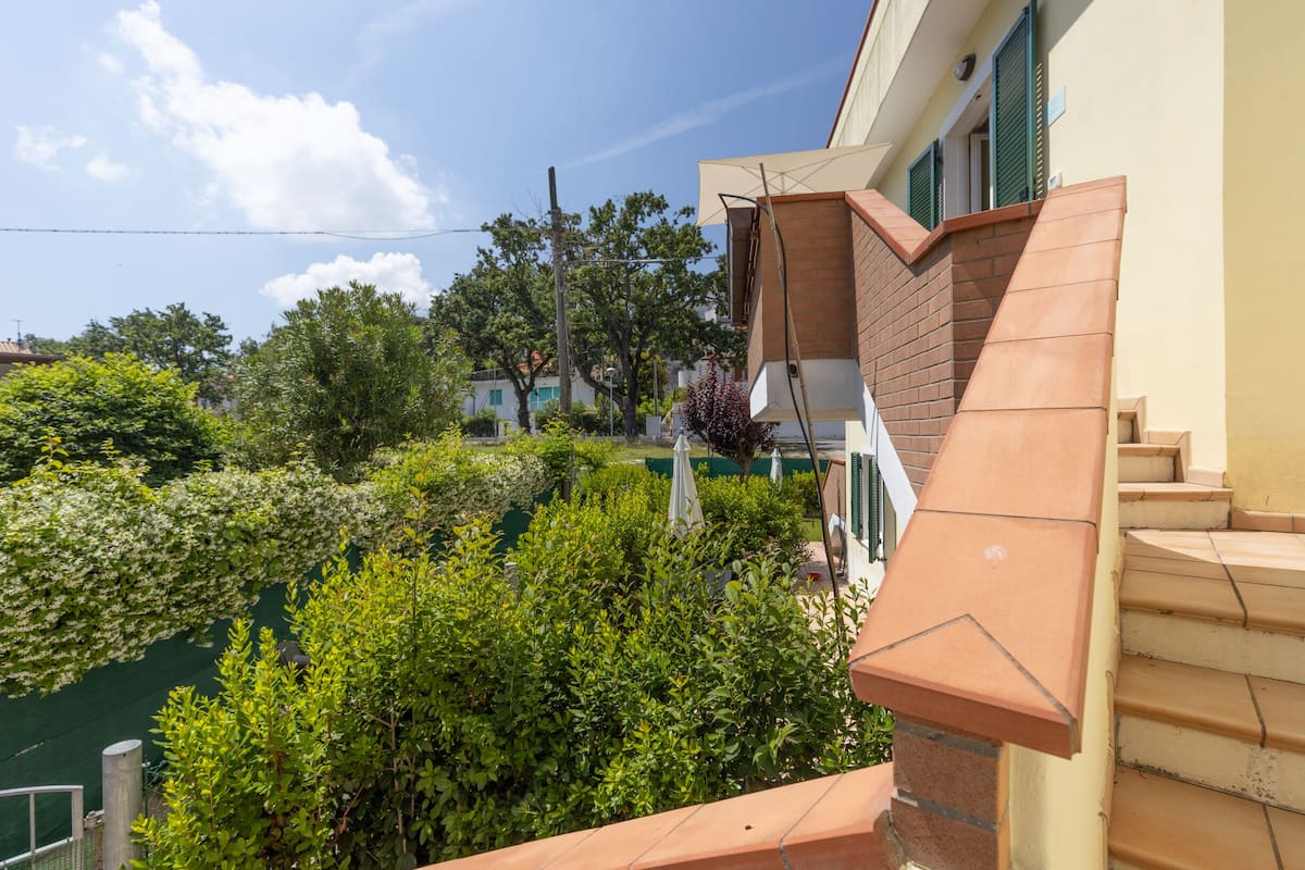 Un immeuble résidentiel avec un escalier en briques, un jardin verdoyant et un ciel dégagé.
