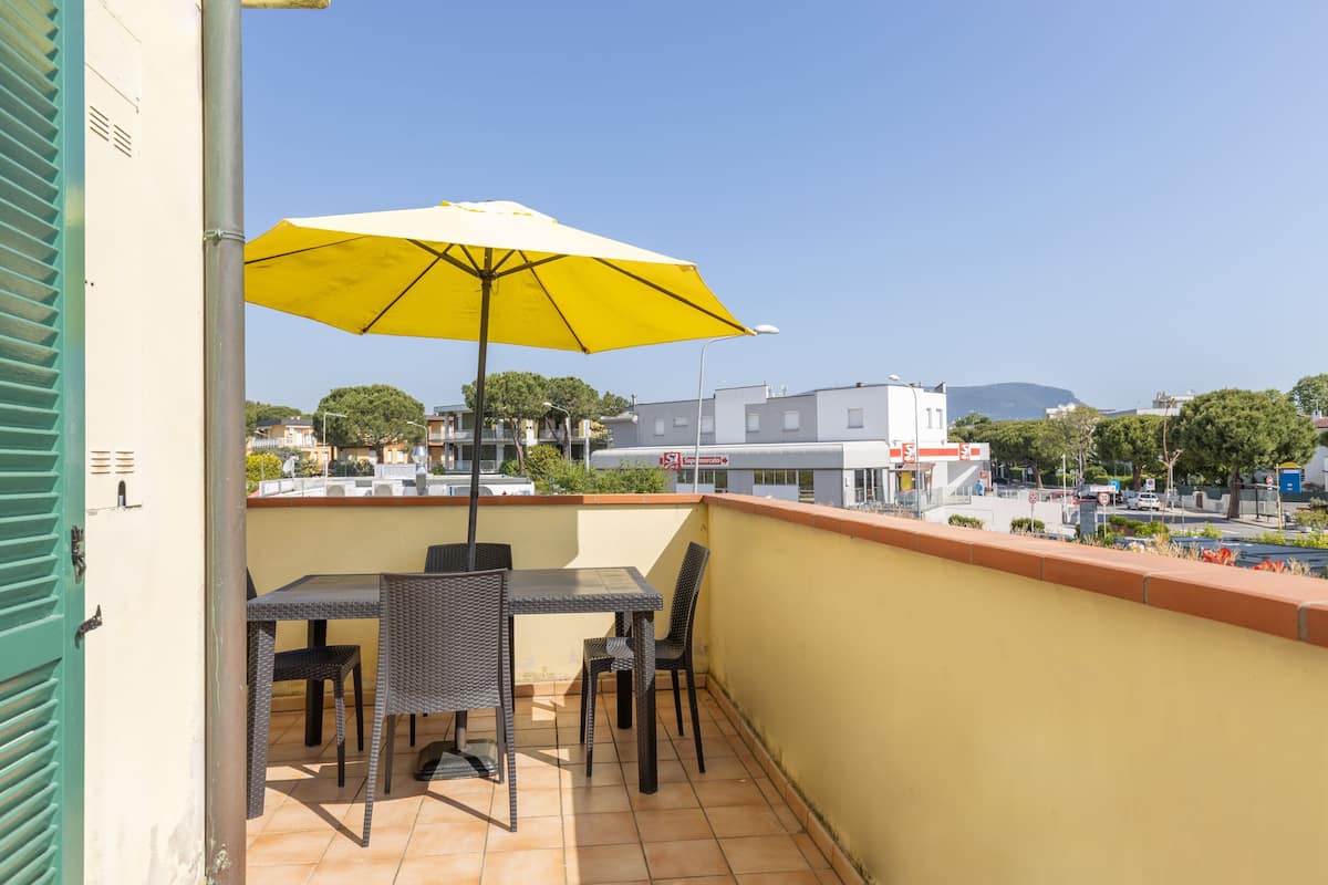 Un balcon avec un parasol jaune, une table et deux chaises.