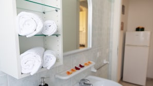 Un baño con repisas de vidrio que sostienen toallas enrolladas, un espejo, un lavamanos y un inodoro.