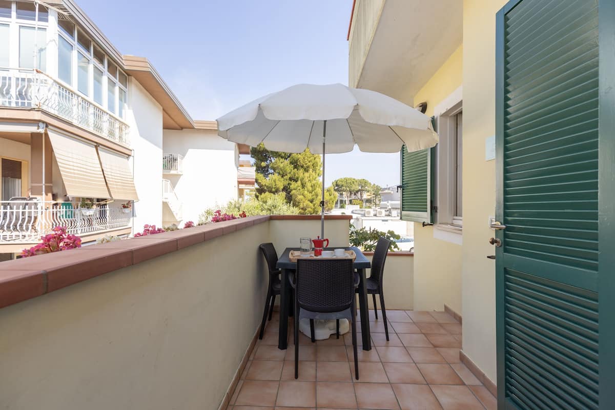 Un balcon avec une table et des chaises, un parasol et une porte verte.
