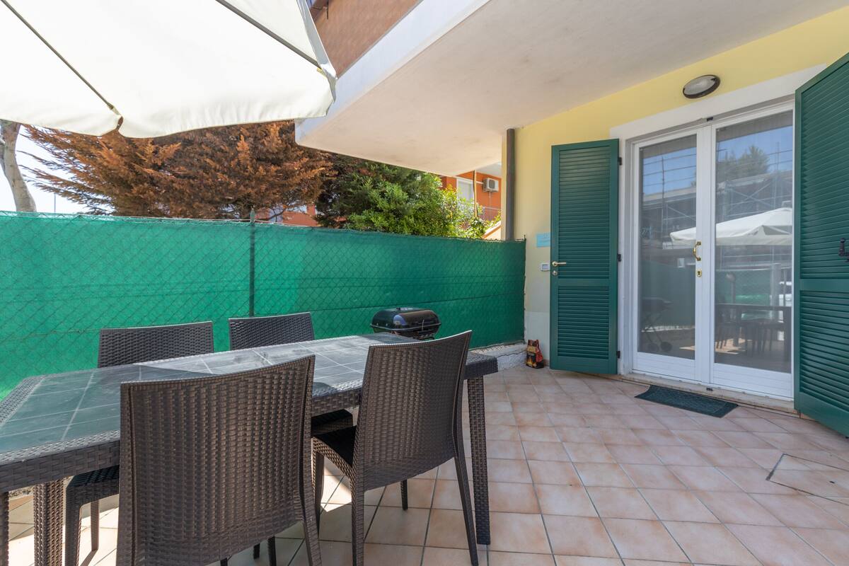 Une terrasse extérieure avec une table et des chaises, un barbecue et une clôture verte.