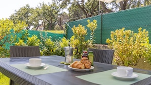 Un espacio al aire libre para comer con una mesa lista para dos personas, que incluye platos, tazas y un croissant.