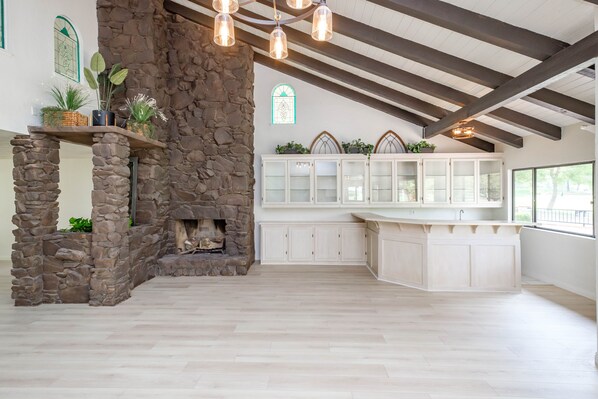 Cozy kitchen with a stone fireplace, high ceiling, and large island.