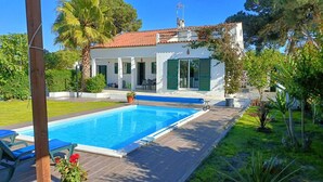 A swimming pool with a wooden deck, surrounded by lush greenery and a white building with green shutters. - A Casa da Lagoa (Lagoa de Albufeira) - 800 da Praia (Sesimbra)