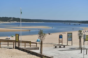 Une plage avec une promenade en bois, un drapeau et des panneaux d’information.