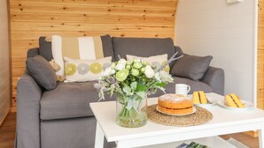 Un salon chaleureux avec un plafond en bois, un canapé gris agrémenté de coussins décoratifs, un vase rempli de fleurs et une table sur laquelle se trouvent un gâteau et des assiettes.