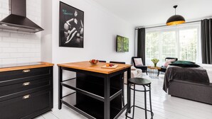 Cozinha moderna com armários pretos, bancada de madeira e fogão embutido. Há uma área de refeições com mesa e cadeiras, e uma janela grande com cortinas.
